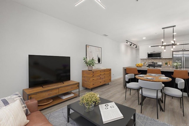 living room featuring baseboards, rail lighting, a notable chandelier, and light wood-style flooring