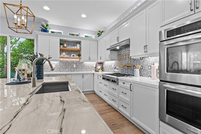 kitchen featuring a sink, white cabinets, double oven, and under cabinet range hood