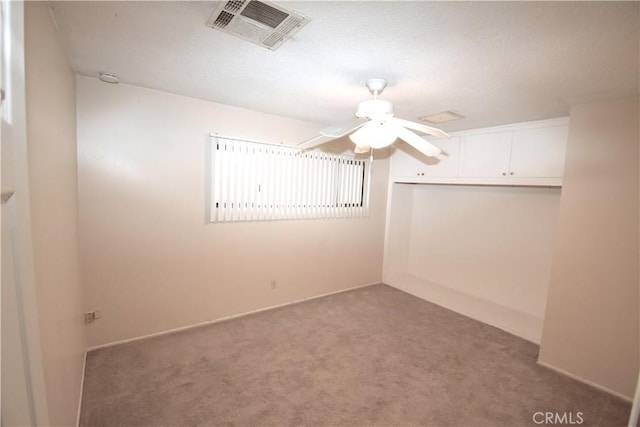empty room featuring a ceiling fan, visible vents, and carpet