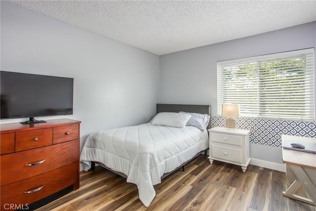bedroom featuring baseboards, a textured ceiling, and wood finished floors