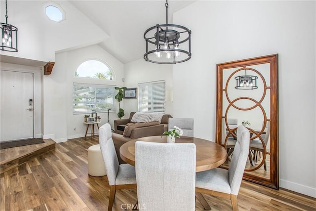 dining area featuring high vaulted ceiling, a notable chandelier, baseboards, and wood finished floors