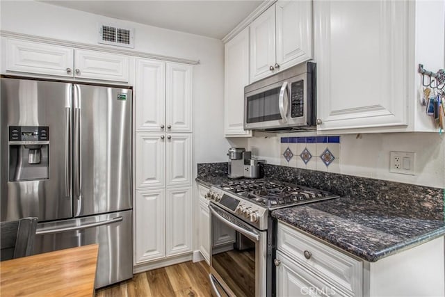kitchen with visible vents, light wood-style floors, white cabinetry, dark stone countertops, and stainless steel appliances