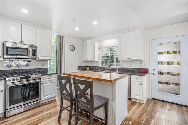 kitchen with a sink, appliances with stainless steel finishes, light wood-type flooring, and wood counters