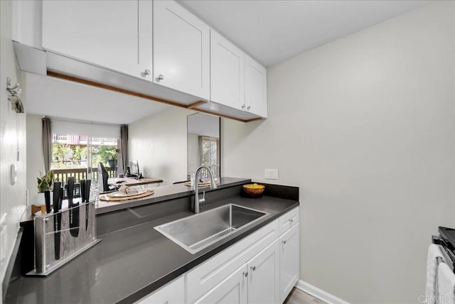 kitchen with white cabinetry, dark countertops, a sink, and electric stove