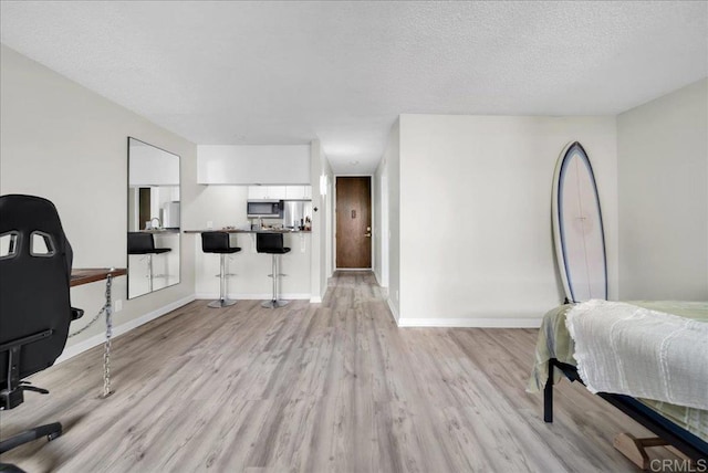 bedroom featuring light wood-style floors, a textured ceiling, and baseboards