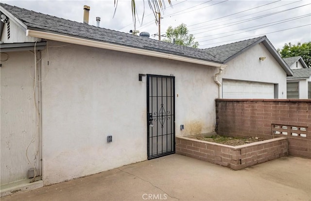 property entrance with an attached garage, a shingled roof, and stucco siding