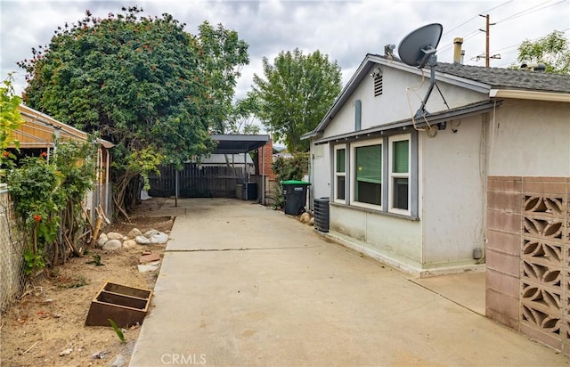 view of side of property with fence, concrete driveway, stucco siding, and cooling unit