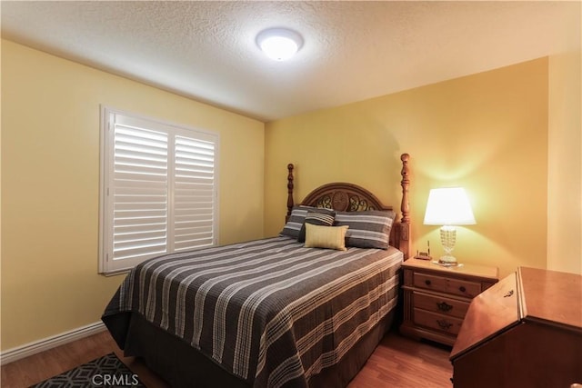 bedroom with baseboards, a textured ceiling, and wood finished floors