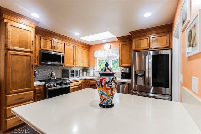 kitchen with brown cabinetry, backsplash, a skylight, light countertops, and stainless steel appliances