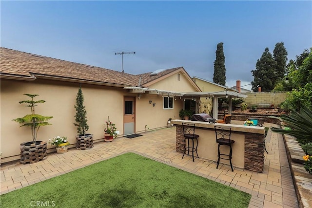 back of property with roof with shingles, stucco siding, outdoor dry bar, and fence