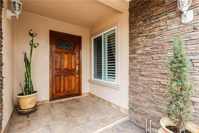 property entrance featuring a porch, stucco siding, and stone siding