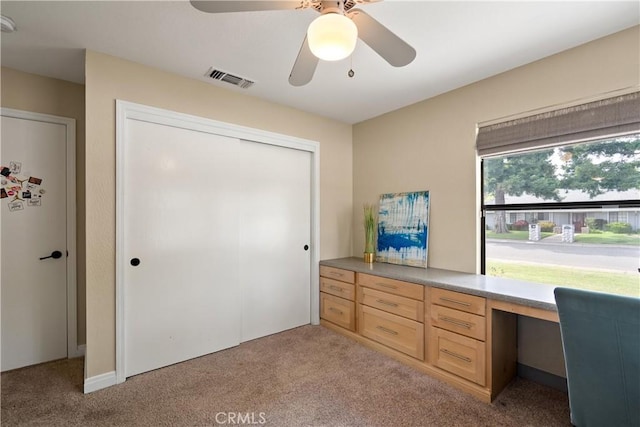 office area featuring visible vents, a ceiling fan, built in desk, and light colored carpet