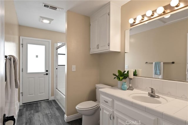 full bathroom with visible vents, wood finished floors, vanity, bath / shower combo with glass door, and toilet