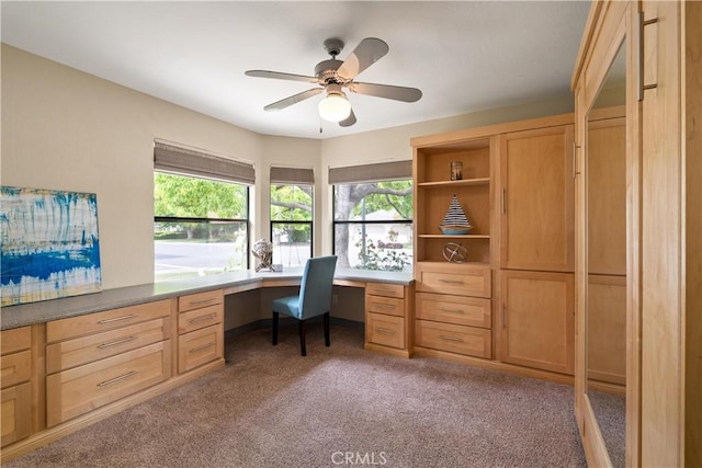 office area featuring light colored carpet, a ceiling fan, and built in desk