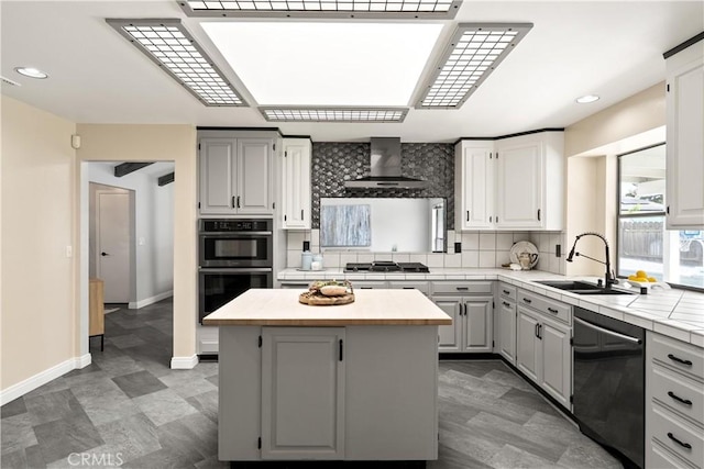 kitchen featuring wall chimney range hood, a sink, dishwasher, backsplash, and multiple ovens