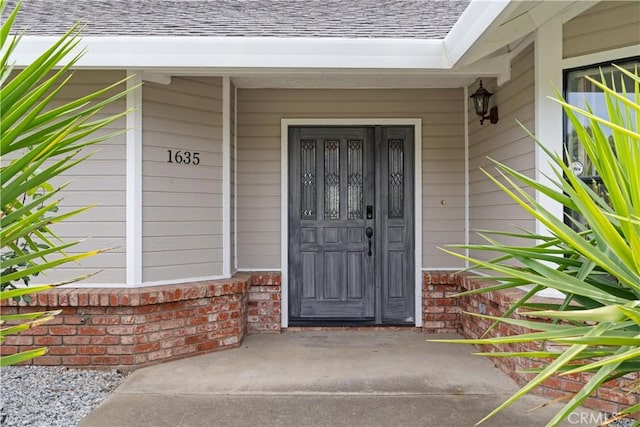 property entrance with brick siding, a shingled roof, and covered porch