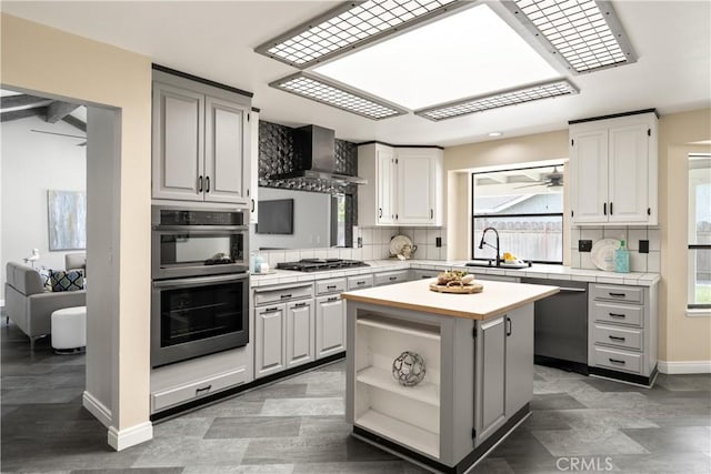 kitchen with appliances with stainless steel finishes, a sink, wall chimney exhaust hood, baseboards, and backsplash