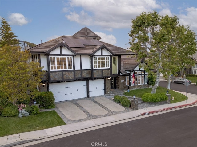 tudor home with a garage, stone siding, stucco siding, roof mounted solar panels, and driveway