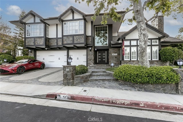 tudor house featuring stone siding, a garage, stucco siding, a chimney, and concrete driveway