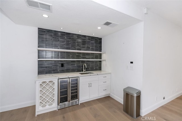 bar featuring a sink, indoor wet bar, light wood-type flooring, wine cooler, and visible vents