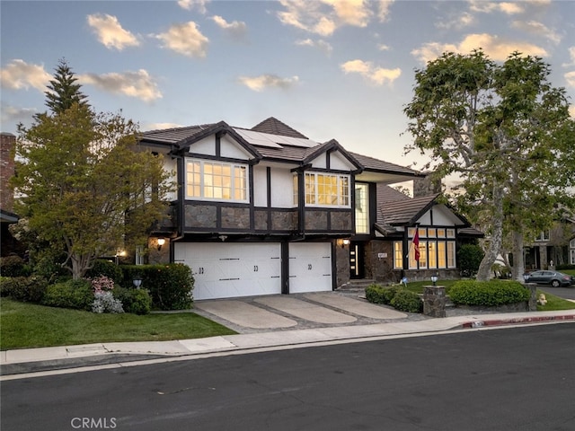 english style home featuring stone siding, stucco siding, concrete driveway, an attached garage, and solar panels