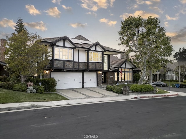 tudor house with roof mounted solar panels, concrete driveway, an attached garage, stone siding, and stucco siding