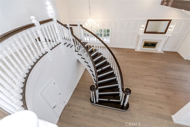 stairs featuring a fireplace with flush hearth, wood finished floors, and a notable chandelier