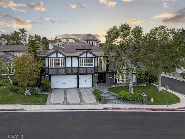 tudor house featuring a garage, stone siding, a tiled roof, concrete driveway, and solar panels