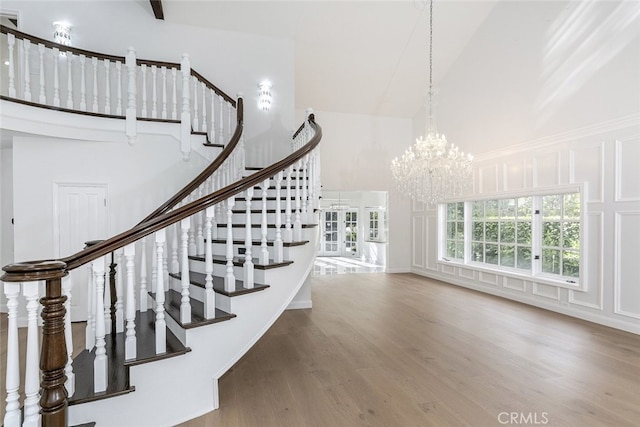 stairway with a towering ceiling, wood finished floors, a chandelier, and a decorative wall