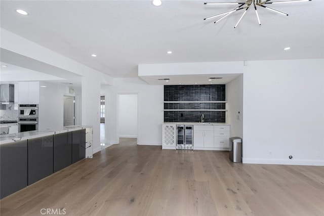 unfurnished living room with indoor wet bar, recessed lighting, light wood-style floors, and wine cooler
