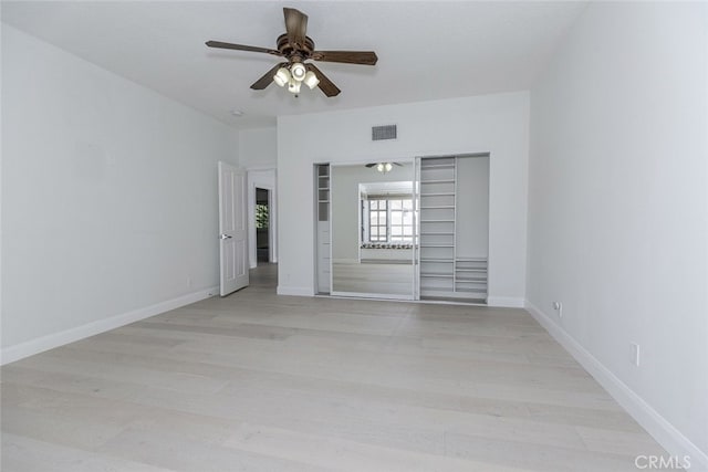 unfurnished bedroom featuring ceiling fan, light wood-style flooring, baseboards, visible vents, and a closet