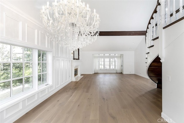 unfurnished living room with a high end fireplace, beam ceiling, baseboards, light wood finished floors, and a chandelier