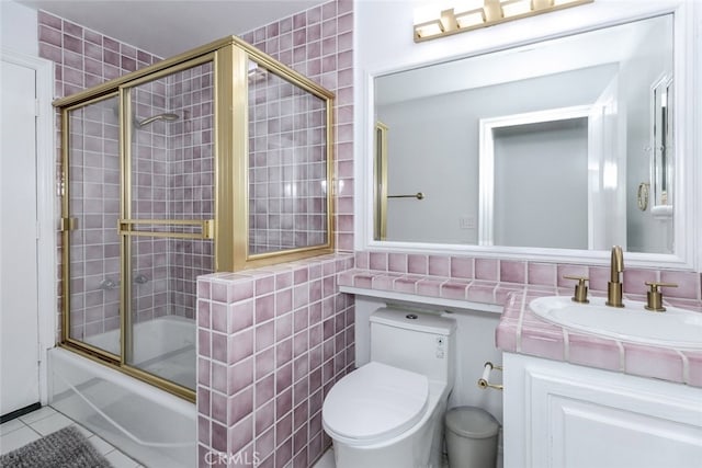 bathroom featuring tile walls, tile patterned flooring, vanity, combined bath / shower with glass door, and toilet