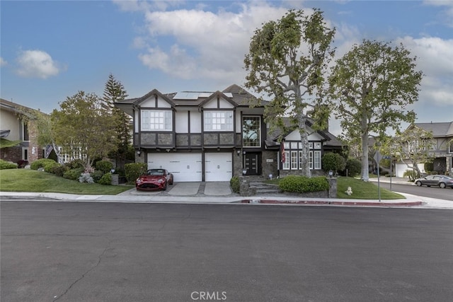 tudor home with a residential view, a garage, stucco siding, roof mounted solar panels, and driveway