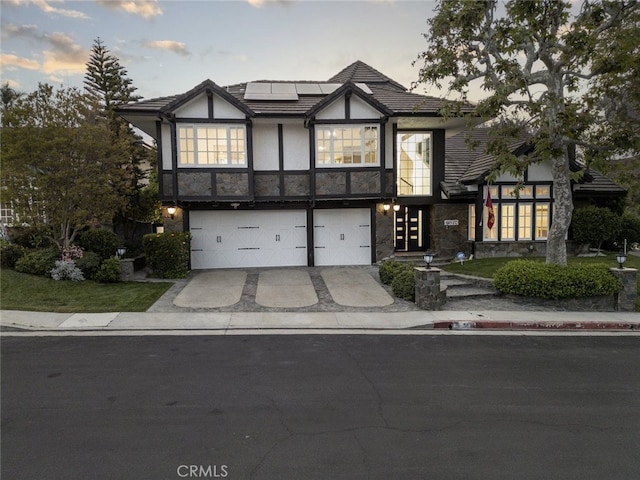 tudor home featuring stone siding, stucco siding, concrete driveway, an attached garage, and solar panels