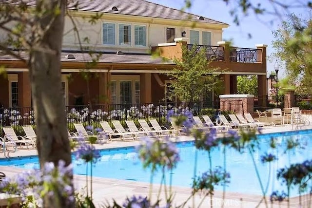 rear view of property featuring a patio, a community pool, fence, and stucco siding