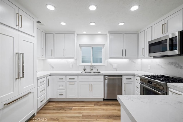 kitchen featuring a sink, light wood-style flooring, white cabinetry, recessed lighting, and premium appliances