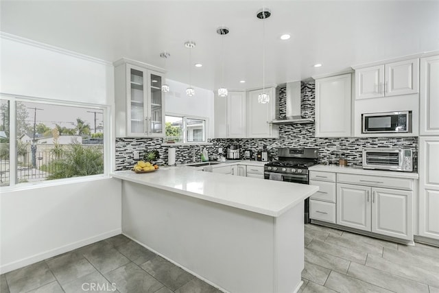 kitchen with wall chimney range hood, appliances with stainless steel finishes, a peninsula, a toaster, and glass insert cabinets
