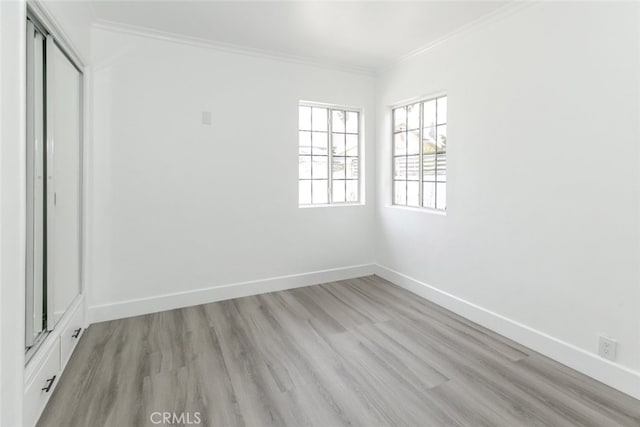 spare room featuring crown molding, light wood-style flooring, and baseboards