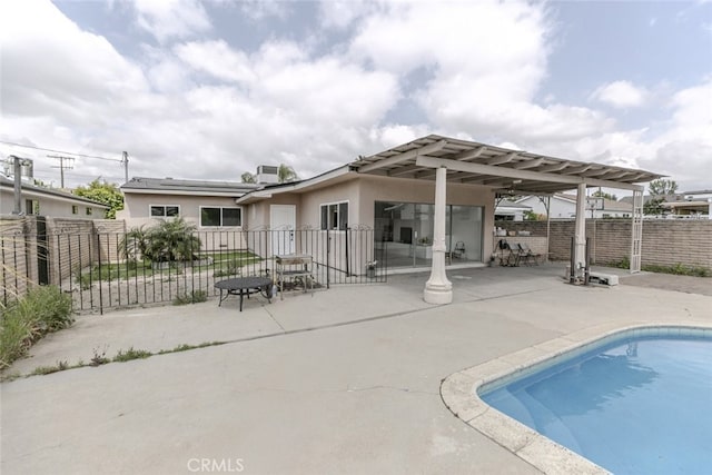 back of house with fence, stucco siding, a fenced in pool, a patio area, and solar panels