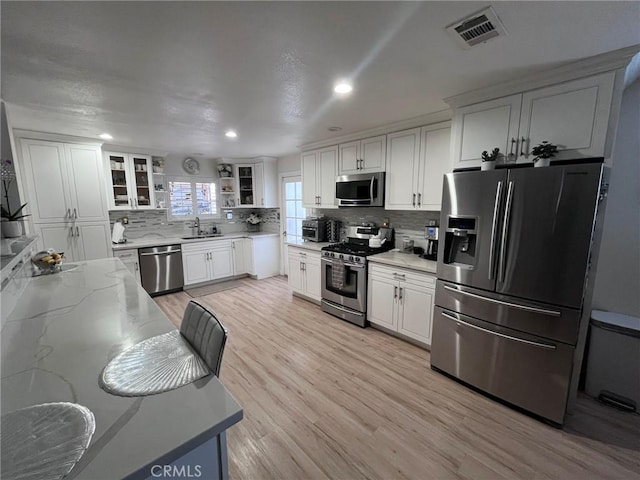 19522 Caney Ave, Carson, CA 90746 - kitchen featuring white cabinets, light wood-style flooring, stainless steel appliances, decorative backsplash, and visible vents
