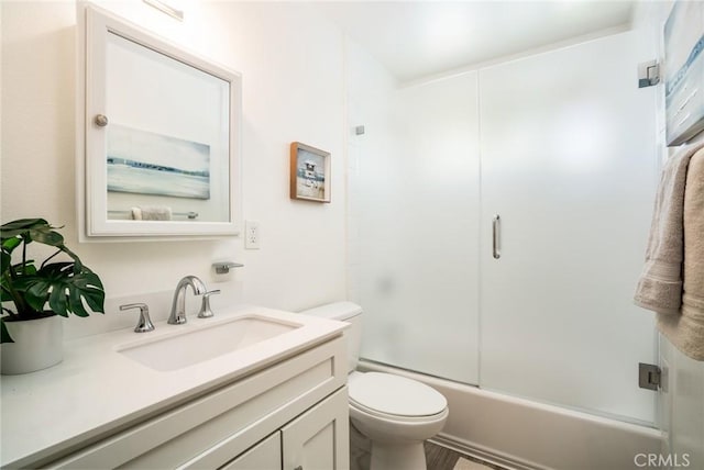 bathroom featuring toilet, combined bath / shower with glass door, and vanity