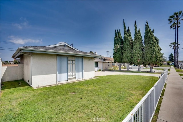 rear view of house with a yard, fence, and stucco siding