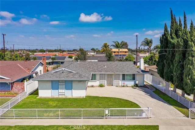 rear view of property with a shingled roof, a fenced front yard, stucco siding, a yard, and driveway