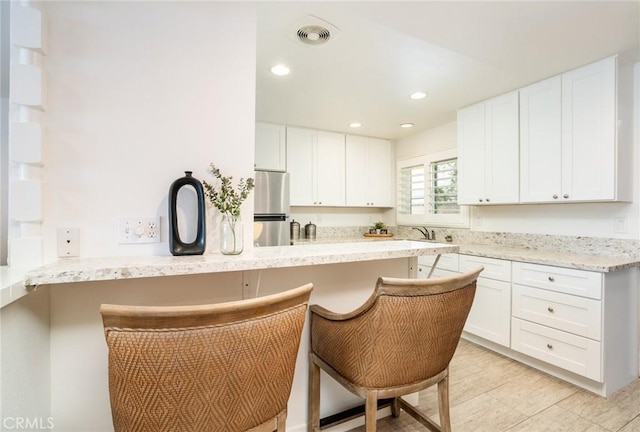 kitchen featuring freestanding refrigerator, white cabinetry, and a peninsula