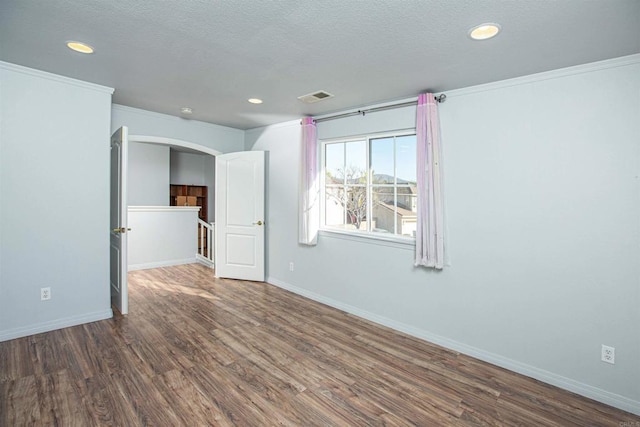 empty room featuring visible vents, arched walkways, baseboards, and wood finished floors