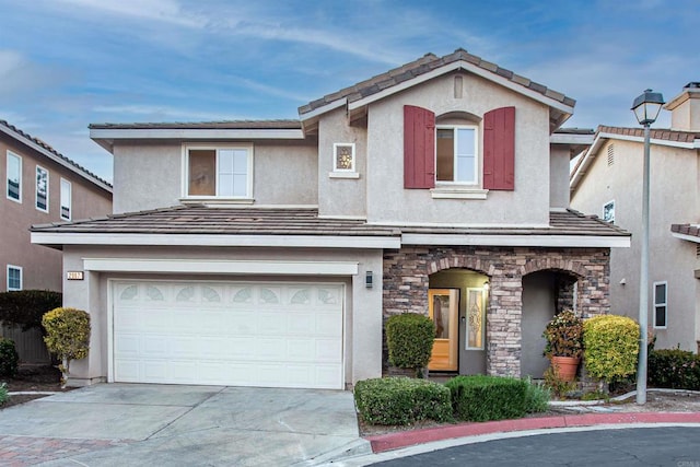 traditional-style house featuring a garage, stucco siding, driveway, and stone siding