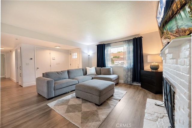 living room featuring light wood-type flooring, baseboards, and a brick fireplace