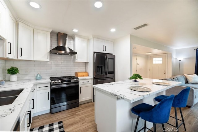kitchen featuring wall chimney range hood, black fridge, gas stove, open floor plan, and visible vents
