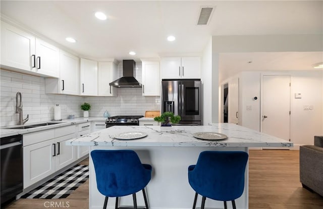 kitchen featuring wall chimney range hood, stainless steel fridge, a sink, a kitchen bar, and dishwashing machine